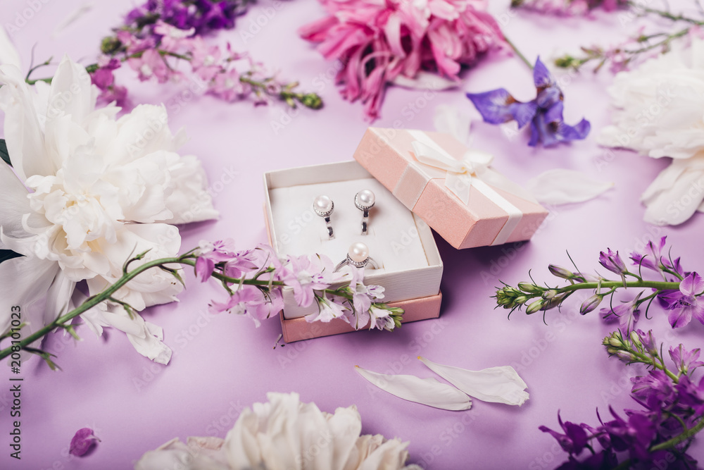 Set of pearl jewellery in gift box with fresh flowers. Silver earrings and ring as a present on purple background. Set of pearl jewellery in gift box with fresh flowers. Silver earrings and ring as a present on purple background.