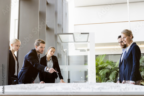 Businessmen and women pointing at architectural model in office