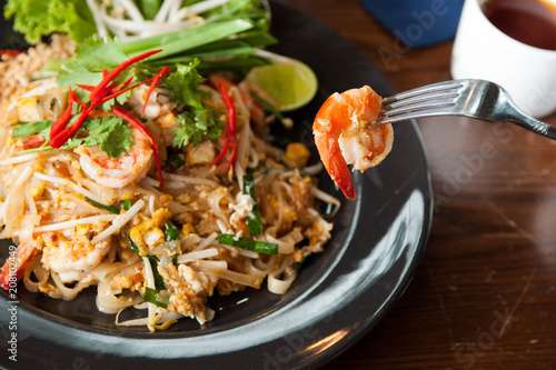 Pad Thai with Shrimp in black plate on wooden table,Using fork to eat shrimp with Padthai lay on wooden table,Thai food for meal time