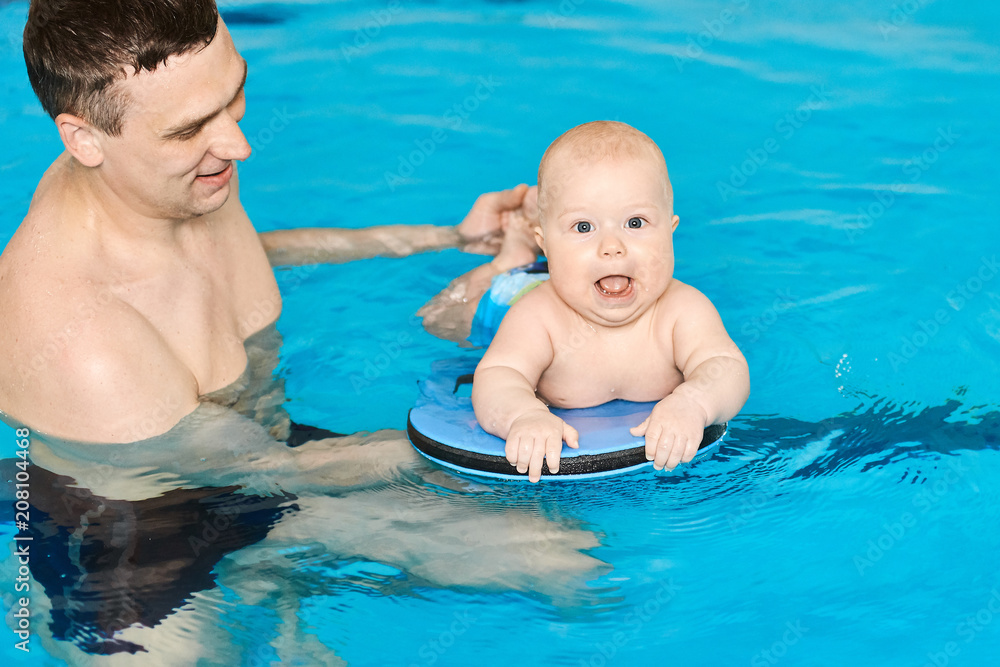 Happy baby boy swimming in water pool with help from father and boards Happy baby boy swimming in water pool with help from father and boards