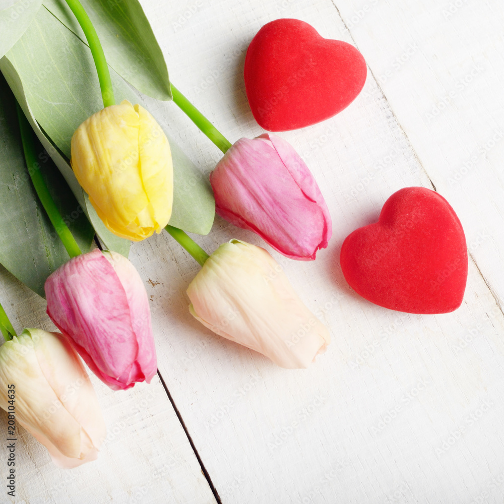 High angle shot of pink rosy and yellow Spring tulip flowers and red hearts on white wooden table