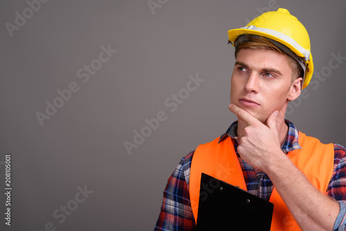 Young handsome man construction worker against gray background
