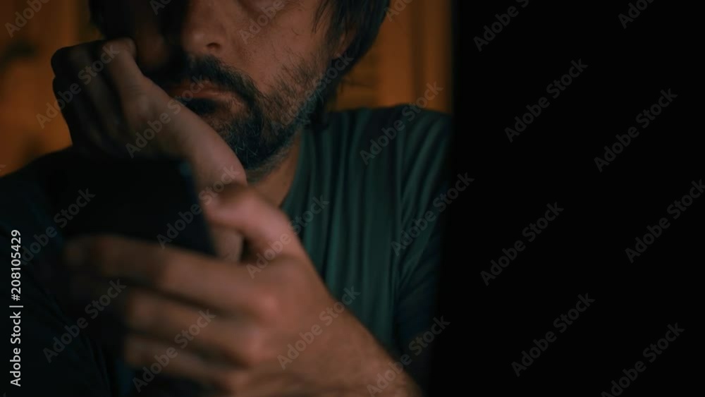 Bored man wasting time using mobile phone in dark home office interior, low key with selective focus Bored man wasting time using mobile phone in dark home office interior, low key with selective focus