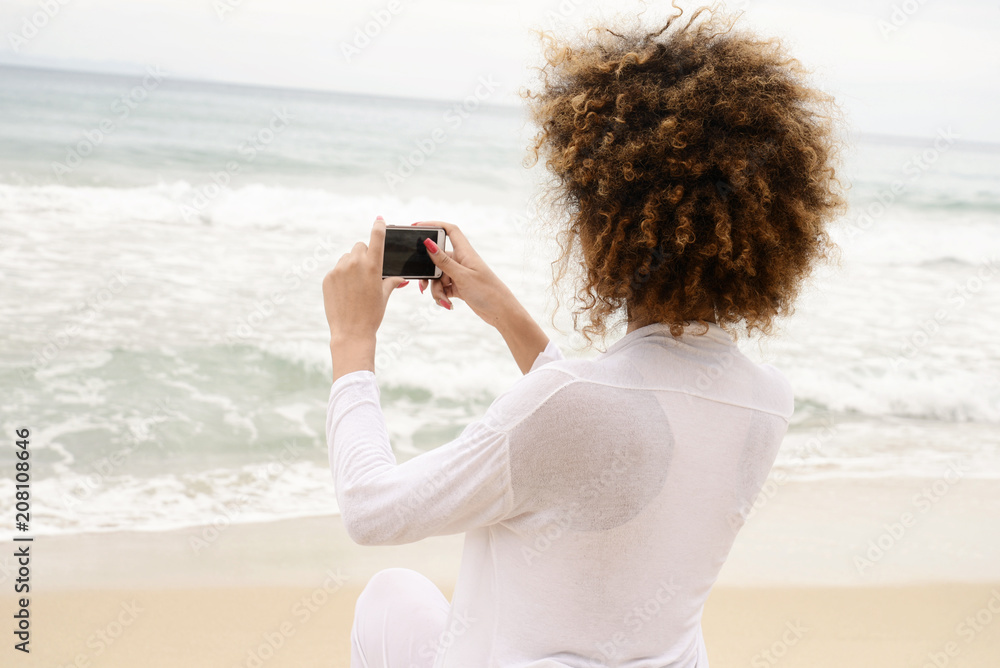 beautiful girl with afro hair and white dress taking photo with smartphone