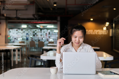 Smiling beautiful woman using laptop computer and pen touching head to thinking new ideas for new business project plan. Businesswoman working on laptop and creating new idea strategy at desk.