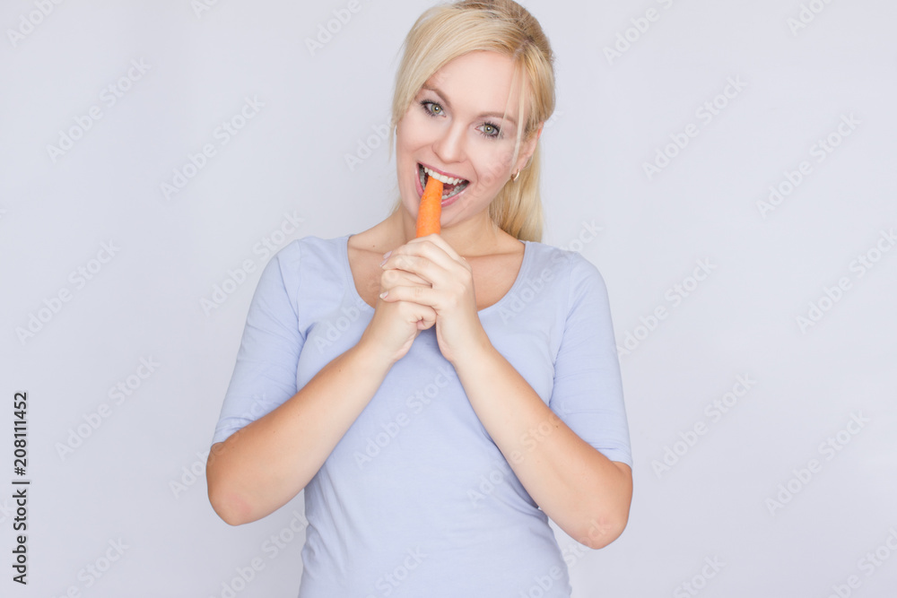 Young blond woman biting young large carrots with her teeth Young blond woman biting young large carrots with her teeth
