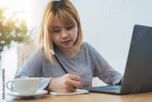 Beautiful young smiling asian woman working on laptop while sitting in a living room at home. Asian business woman working in her home office. Enjoying time at home.