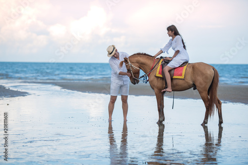 Happy young couple with enjoying together, woman riding a hose and her boyfriend to lead a horse on the summer beach, romantic couple spending time concept.