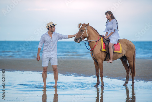 Happy young couple with enjoying together, woman riding a hose and her boyfriend to lead a horse on the summer beach, romantic couple spending time concept. © May Chanikran