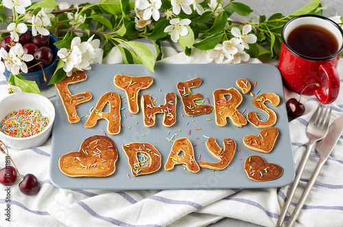 Special Father's Day breakfast. Alphabet Pancakes with sprinkles, cherries and cup of tea on a gray concrete background