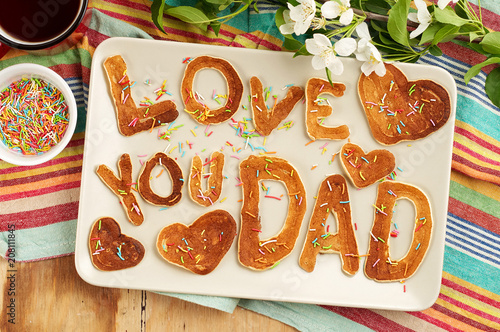 Special Father's Day breakfast. Alphabet Pancakes with sprinkles, cherries and cup of tea on wooden background