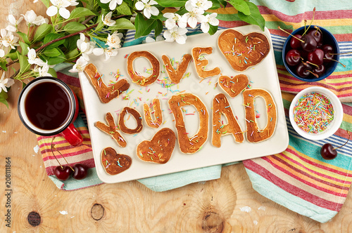 Special Father's Day breakfast. Alphabet Pancakes with sprinkles, cherries and cup of tea on wooden background