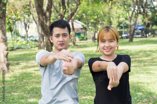 Asian sweet couple warm up their bodies by stretching arms before morning jogging exercise in the park surrounded with nature and warm light sunshine. lover couple exercise together outdoor with love.