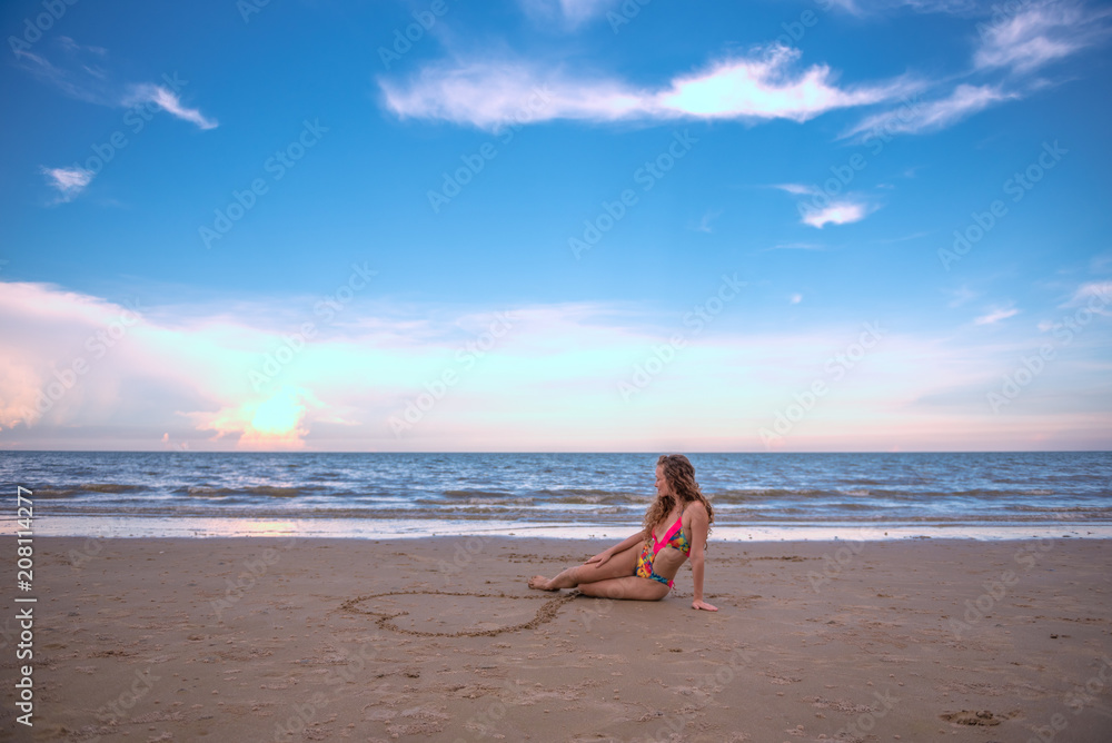 Portrait happy woman sitting in the Heart shape drawing on the sand at the beach with enjoying and refreshing, summer beach relaxing time concept.