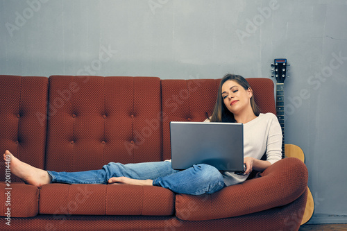 Young woman lies on sofa with laptop. photo