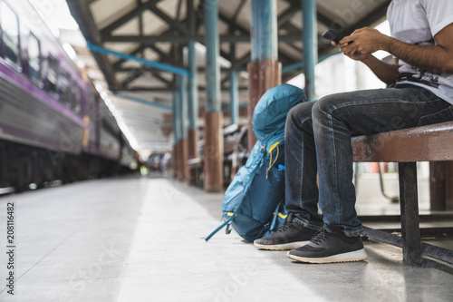 Backpack and hat at the train station with a traveler, Young man sitting with using smartphone at the train station, Summer holiday and travel concept