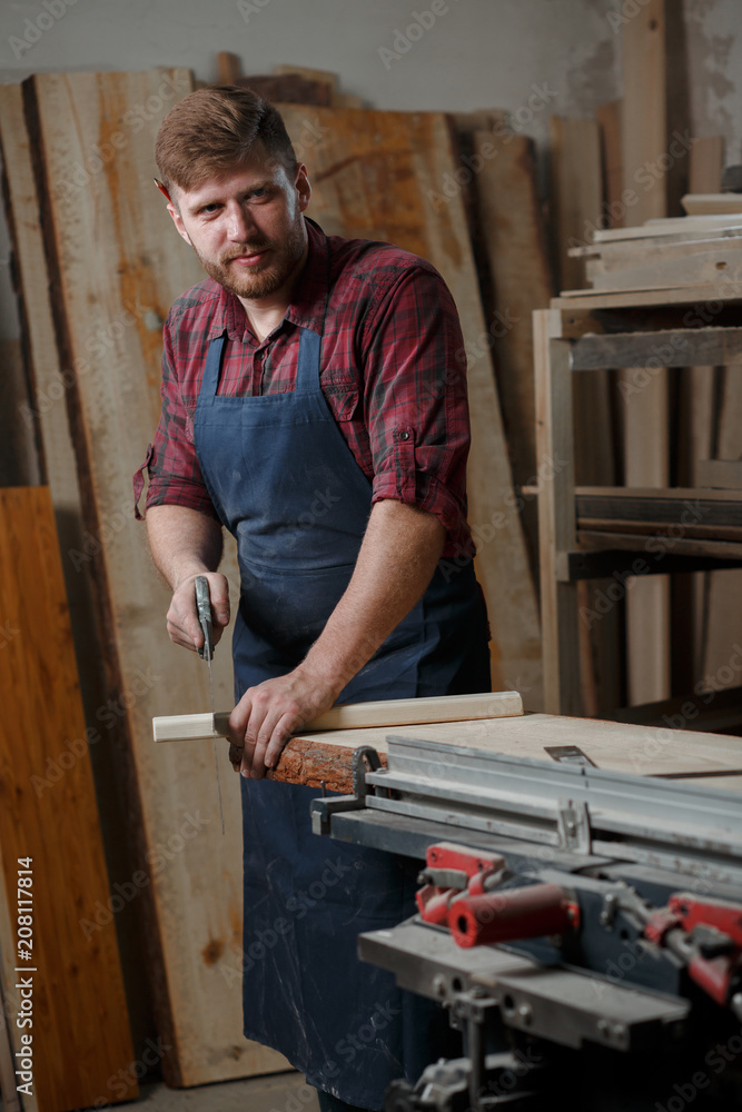 Master carpenter saws board with hacksaw in workshop