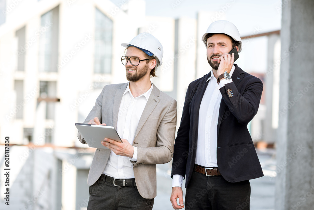 Two engineers working with tablet standing on the structure site with a new house on the background Two engineers working with tablet standing on the structure site with a new house on the background