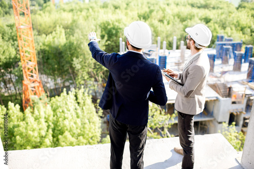 Two engineers or architects supervising the process of residential building construction standing on the structure outdoors