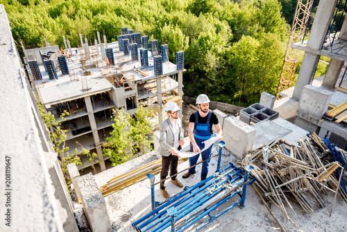 Top view on the construction site of residential buildings during the construction process with two workers standing with drawings