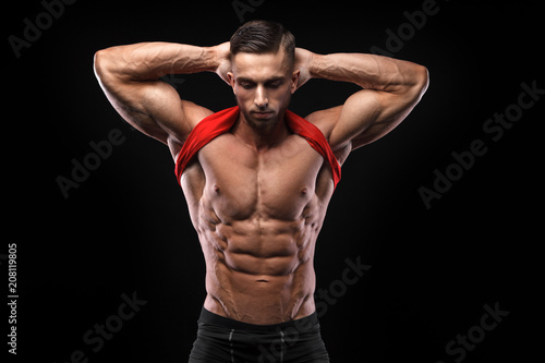 Cute young sports man in red t-shirt shows relief abdominal muscles in gym