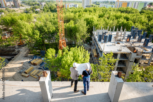Top view on the construction site of residential buildings on the green area with two workers looking on the construction process