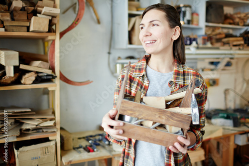 Beautiful woman smiling and looking away while holding wooden box with carpenter tools. 