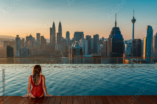Asian travel and vacation. Young woman enjoying the city view from roof top swimming pool.