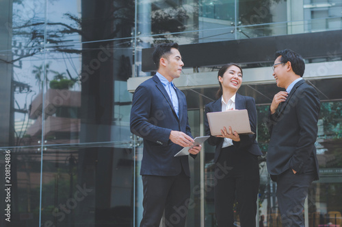 two attractive business man and a business woman talking and discussion together in business working at outdoor in front of modern building office in city. business teamwork leadership concept.