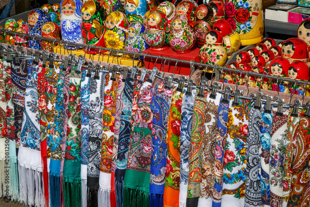 Many multicolored fabric scarves and painted dolls - matryoshkas, so-called Russian souvenirs, lie on the counter in a street store and wait for tourists