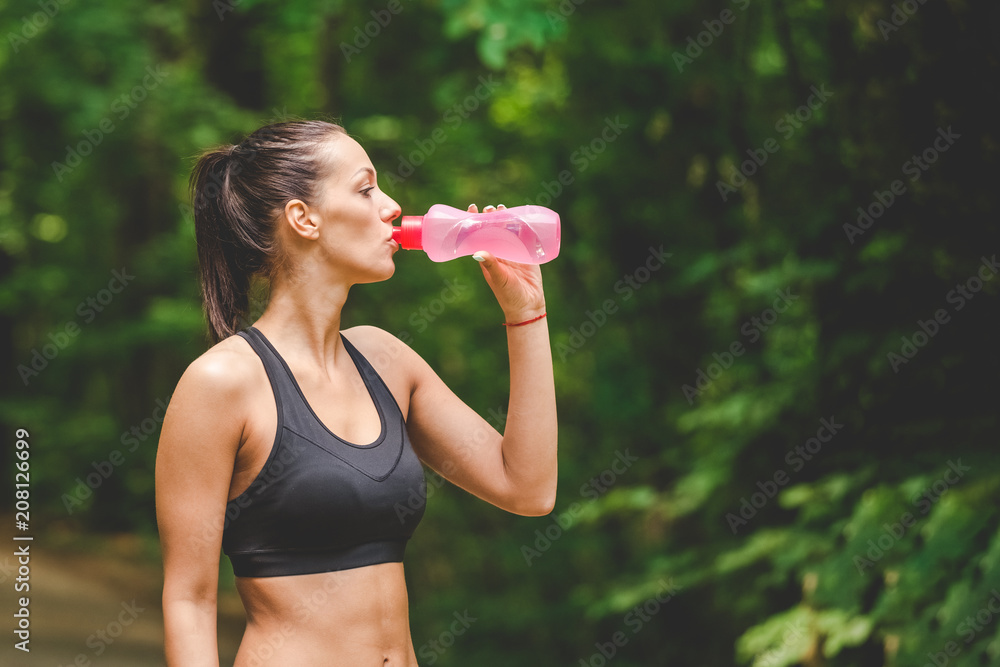 Beautiful sportswoman runner drinking water from bottle next to running track outdoors. Beautiful sportswoman runner drinking water from bottle next to running track outdoors.