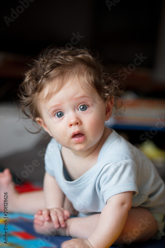 little curly baby boy sitting at floor in loft flat.