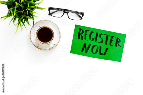 Membership concept. Template for registration. Register now hand lettering iconon word desk with glasses, coffee, plant on white background top view space for text photo