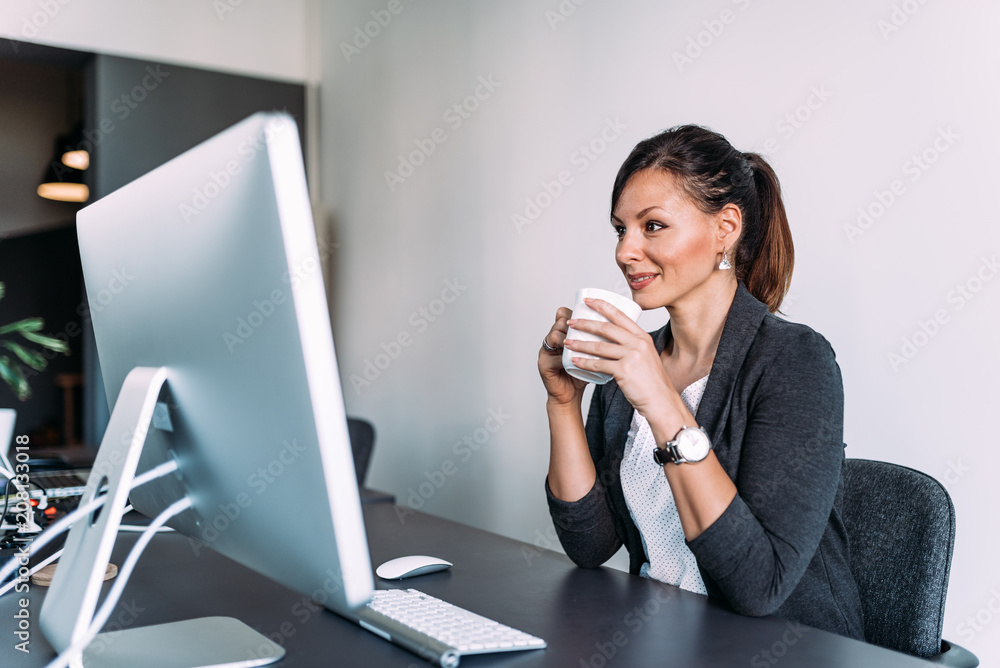 Young attractive woman at modern office desk drinking coffee. Young attractive woman at modern office desk drinking coffee.