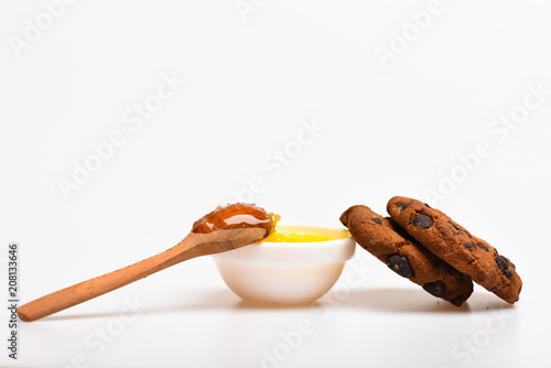 Cookies with chocolate drops and bowl with honey and wooden spoon, white background. Healthy sweets concept. Cookies and honey tasty sweets. High calorie food with honey, close up