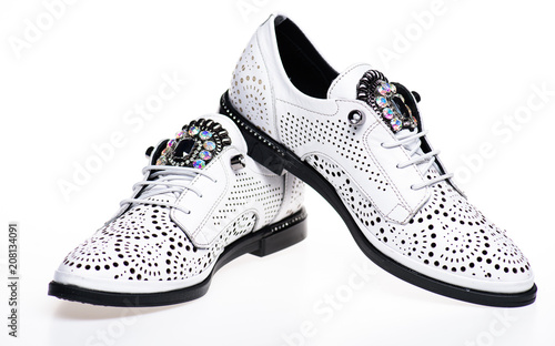 Shoes made out of white leather on white background, isolated. Pair of fashionable comfortable oxfords shoes. Footwear for women on flat sole with perforation and rhinestones. Modern shoes concept.