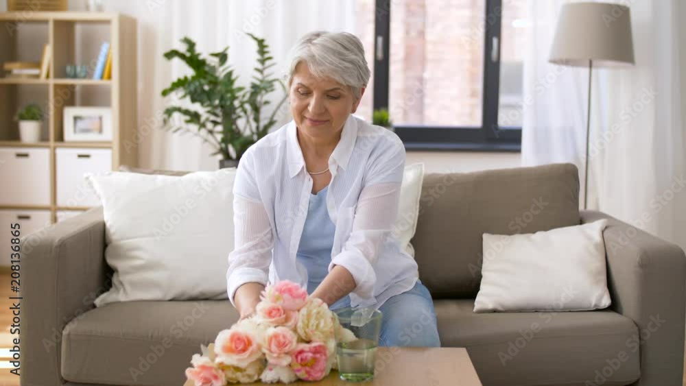 holidays, age and people concept - happy senior woman putting flowers to vase at home holidays, age and people concept - happy senior woman putting flowers to vase at home