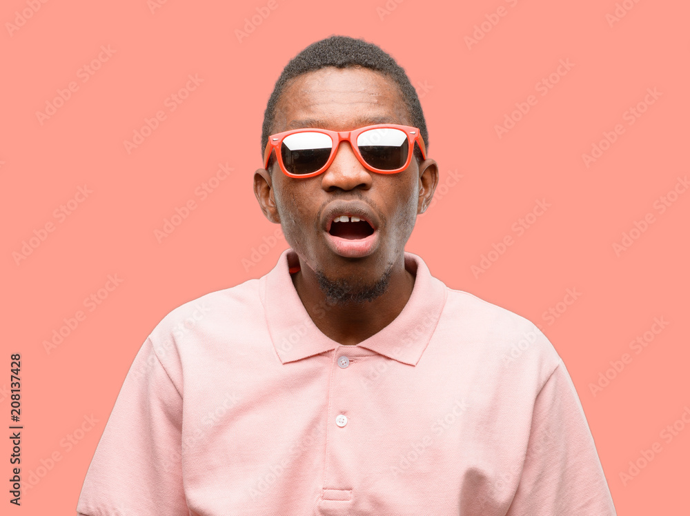 Obraz premium African black man wearing sunglasses scared in shock, expressing panic and fear