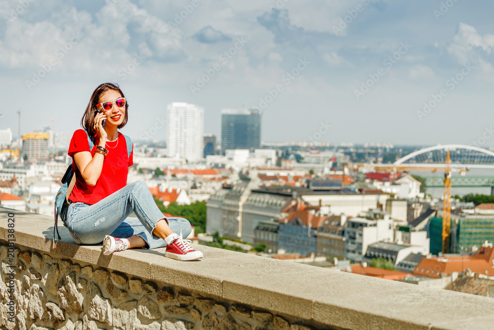 Happy woman in red talking on a smart phone at the background of modern European city
