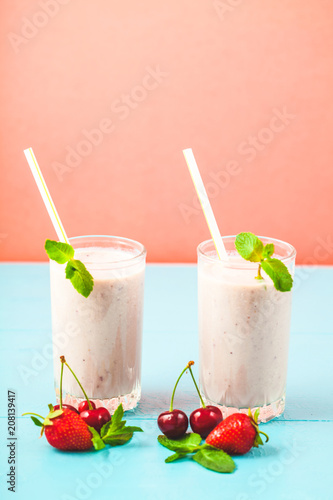 Two glasses of milk smoothies with cherries, strawberries, banana and mint on bright background Concept of a healthy lifestyle. Place for copy space Tasty and healthy weight loss