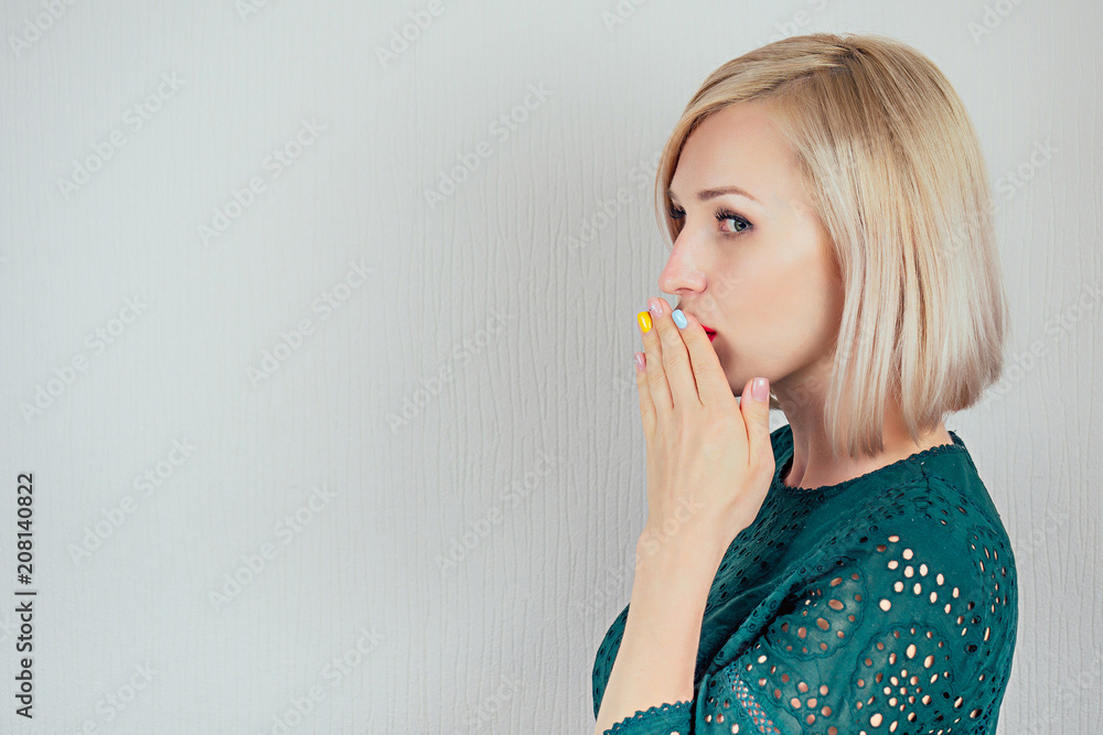 portrait of a young attractive woman with blonde hair and makeup whispers a secret (mystery) in the studio on a grey background. the concept of gossip and confidentiality portrait of a young attractive woman with blonde hair and makeup whispers a secret (mystery) in the studio on a grey background. the concept of gossip and confidentiality