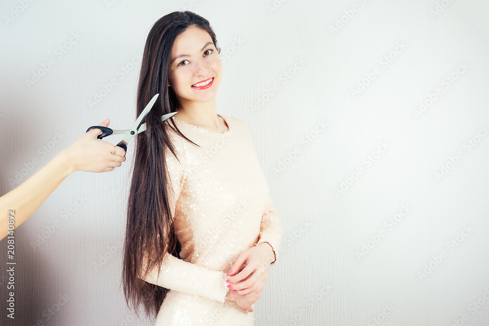 Obraz premium portrait of a young attractive brunette woman with long black hair and makeup in a pink dress shears with scissors haircut in the hairdresser's (barbershop)