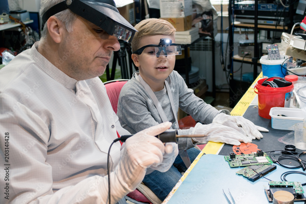 Engineering teacher teaching small boy to use soldering iron on computer part. Engineering teacher teaching small boy to use soldering iron on computer part.