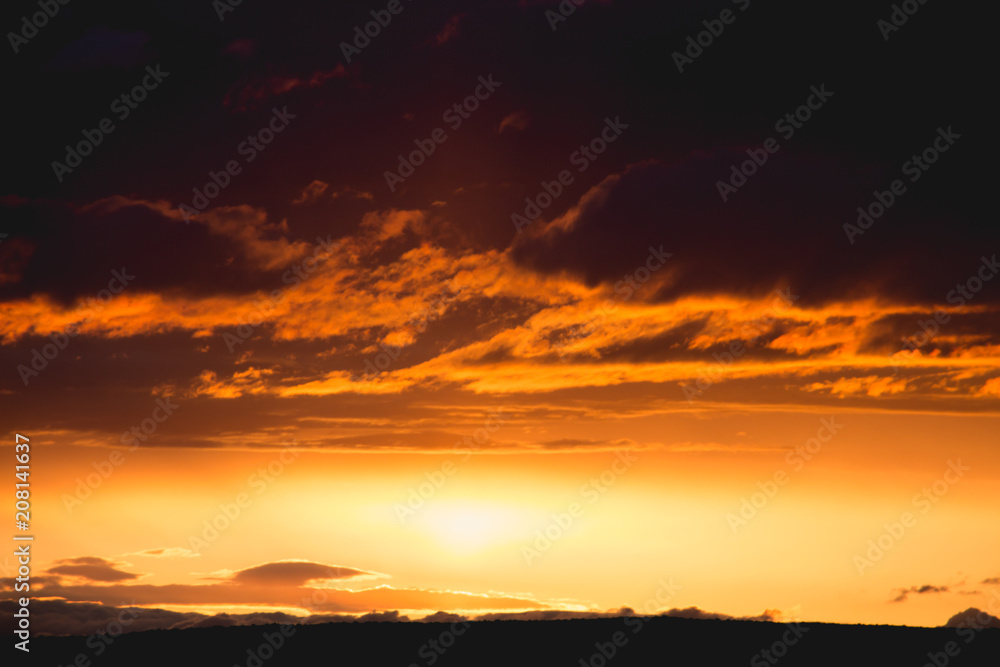 orange clouds and golden sun beam at sunset horizon