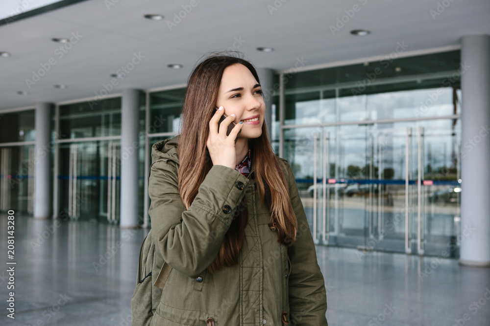 Young beautiful tourist girl at the airport or near the shopping center or the station calls a taxi or talking on a cell phone or talking to friends using a mobile phone Young beautiful tourist girl at the airport or near the shopping center or the station calls a taxi or talking on a cell phone or talking to friends using a mobile phone