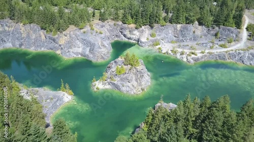 A cinematic aerial drone shot flying over a beautiful, tropical green quarry lake on an island off the coast of Powell River, British Columbia. photo