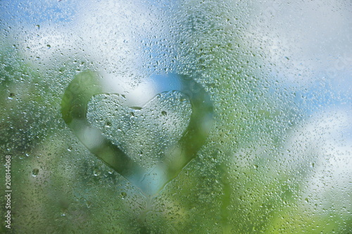 summer rain drops on window glass background texture. the heart is drawn with a finger on the glass.