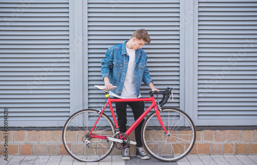 Stylish young man with a bike in which the pierced wheel is standing against the background of the wall. Hipster cyclist is standing against the back of the wall with a bicycle in his hands