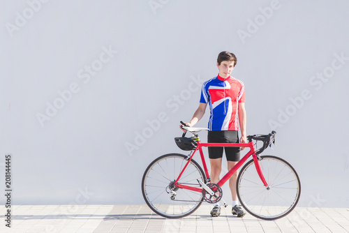 Portrait of a cyclist athlete standing with a red road velosiped on a background of a gray wall and looking into the camera. Sports concept