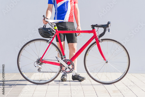 Road red bike and cyclist in bicycle clothes on the background of a white wall. Sports concept. Bicycle and athlete close-up.